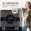 A woman holds a coffee mug next to a coffee maker with a timer display. Produktbild-Vorschau