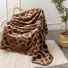 A brown blanket with a geometric pattern is draped over a chair, with a fluffy white rug underneath and a plant in a basket to the side. Podgląd zdjęcia produktu