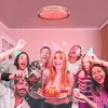 A group of friends celebrating a birthday with sparklers and a cake, under a pink-lit ceiling light. Náhled obrázku produktu