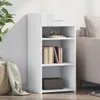 A white sideboard with shelves and a drawer, placed against a white wall next to a sofa. Voir les images du produit
