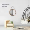 A round mirror with a wooden frame hangs on a white wall, next to a hanging chair and wooden crates with plants. Produktbild-Vorschau