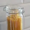 A close-up shot of a glass jar filled with spaghetti, with a white tiled background. Produktbild-Vorschau