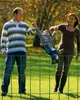 A family is playing with a child in a park, with a fence in the foreground. Produktbild-Vorschau