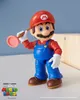 A Mario action figure holding a plunger, set against a light blue background with a wooden object in the background. Anteprima dell’immagine prodotto