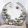 A black metal plant stand with multiple shelves, arranged in a circular design, is shown indoors with plants and decorative items. Anteprima dell’immagine prodotto