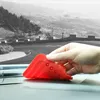 A hand holding a red silicone phone holder on a car dashboard with a scenic black and white background. Produktbild-Vorschau