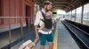 A man with a baby in a carrier at a train station. Náhled obrázku produktu