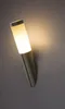 A modern wall lamp with a frosted glass shade and a brushed metal base is mounted on a gray wall. Anteprima dell’immagine prodotto