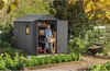 A woman is organizing items inside a gray garden shed. The shed is surrounded by lush greenery and garden beds. Náhled obrázku produktu