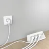 A white power strip with multiple plugs and USB ports is connected to a wall outlet. The power strip is placed on a wooden surface next to a light gray wall. Produktbild-Vorschau