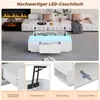 A modern living room scene featuring a white LED couch table with its top lifted, revealing storage and a drawer. The table is placed in front of a sectional sofa and a fireplace. Voir les images du produit