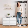 A woman stands next to a white dresser with a height chart on the right. Podgląd zdjęcia produktu