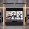A modern living room with a large projection screen displaying a fitness class. The room features a sleek media console and minimalist decor. Podgląd zdjęcia produktu
