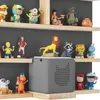 A collection of children's toys and figures displayed on shelves, with a gray speaker device in the foreground. Produktbild-Vorschau