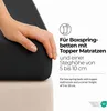 A hand is shown pressing down on a black fitted sheet that is covering a mattress topper. Produktbild-Vorschau
