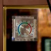 A close-up of a hygrometer mounted on what appears to be a mirror or a display case. Produktbild-Vorschau