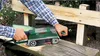 A person is using a Bosch belt sander to sand a wooden bench outdoors. Podgląd zdjęcia produktu