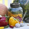 A collection of fresh vegetables and a large plastic jar filled with pickled vegetables. Produktbild-Vorschau