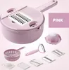 A pink multi-functional vegetable cutter set with various attachments and a colander, displayed against a light pink background. Voir les images du produit