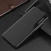 A black flip case for a smartphone is displayed on a dark surface, with a notebook in the background. Produktbild-Vorschau