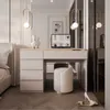 A bedroom scene featuring a vanity desk with a laptop, a stool, and a pair of high heels. Produktbild-Vorschau