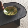 A close-up of a black oval coffee table with a decorative bowl and dried flowers on it, placed on a rug. Produktbild-Vorschau