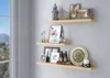 Three wooden shelves mounted on a gray wall, displaying various decorative items and framed pictures. Produktbild-Vorschau