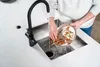 A person is rinsing food scraps from a plate into a kitchen sink with a garbage disposal. Produktbild-Vorschau
