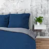 A close-up view of a bed with dark blue bedding and pillows. Produktbild-Vorschau