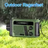 A green and black emergency radio is placed on wet grass, with rain falling in the background. Produktbild-Vorschau