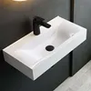 A modern white ceramic sink with a black faucet mounted on a dark gray wall. Produktbild-Vorschau