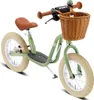 A green balance bike with a brown seat and handlebars, and a wicker basket on the front, is shown against a white background. Náhled obrázku produktu