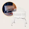A baby bassinet with a mosquito net is shown, with a close-up inset of the bassinet in use with a baby and adult feet visible. Anteprima dell’immagine prodotto