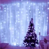 A decorated Christmas tree stands in front of a window with string lights. Náhled obrázku produktu