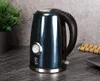 A dark blue electric kettle with a thermometer is placed on a dark countertop next to a potted plant and a bamboo mat. Podgląd zdjęcia produktu