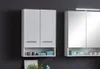Two white bathroom cabinets are shown against a dark gray wall. The cabinet on the left has two doors and an open shelf below, containing towels and containers. The cabinet on the right has mirrored doors and an open shelf below, holding decorative items a Produktbild-Vorschau