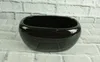 A black oval ceramic planter sits on a white brick surface. Produktbild-Vorschau