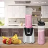 A smoothie maker with a filled blending cup and a separate travel cup, placed on a wooden table in a kitchen setting. Produktbild-Vorschau