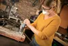 A woman is working on a metal object in a workshop. Produktbild-Vorschau