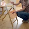 A person is demonstrating how to adjust the seat of a high chair by sliding an orange cushion into place. Voir les images du produit