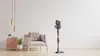 A cordless vacuum cleaner stands in a minimalist living room setting next to a pink armchair. Voir les images du produit