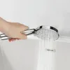 A hand holding a silver shower head with water spraying from it into a bathtub. Produktbild-Vorschau