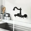 A black wall-mounted faucet with water running into a sink. Produktbild-Vorschau