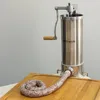 A stainless steel sausage stuffer with a wooden handle is shown on a wooden cutting board, with a coiled sausage emerging from the nozzle. Produktbild-Vorschau