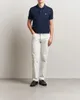 A man wearing a navy blue Lacoste polo shirt and white pants, standing against a white background. Produktbild-Vorschau