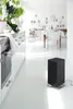A modern, minimalist kitchen and dining area with a black air purifier in the foreground. Podgląd zdjęcia produktu