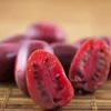 A close-up of halved red fruits with black seeds, arranged on a bamboo mat. Produktbild-Vorschau
