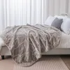 A beige blanket with a geometric pattern is draped over a bed with white pillows and a black and white patterned pillow. Podgląd zdjęcia produktu