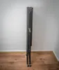 A folded black metal rack with wheels stands against a white wall on a wooden floor. Produktbild-Vorschau