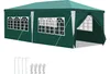 A green tent with white window frames and white curtains, shown from a side angle. Stakes and ties are laid out in front of the tent. Produktbild-Vorschau